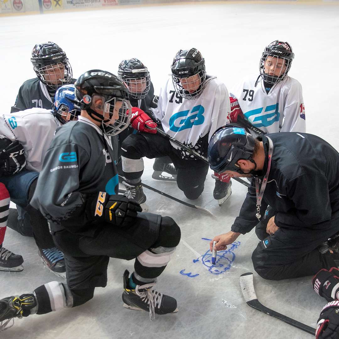 Coach erklärt jungen Spielern im Camp eine Übung auf dem Eis